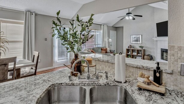 A modern kitchen with a double sink, a dining area with a wooden table and chairs, and a living area with a sofa and a fireplace. - Splash & Play Hideaway: Pool House + Game Room/Gym (Lewisville)