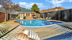A backyard with a swimming pool, a hammock, and a wooden fence. - Splash & Play Hideaway: Pool House + Game Room/Gym (Lewisville)