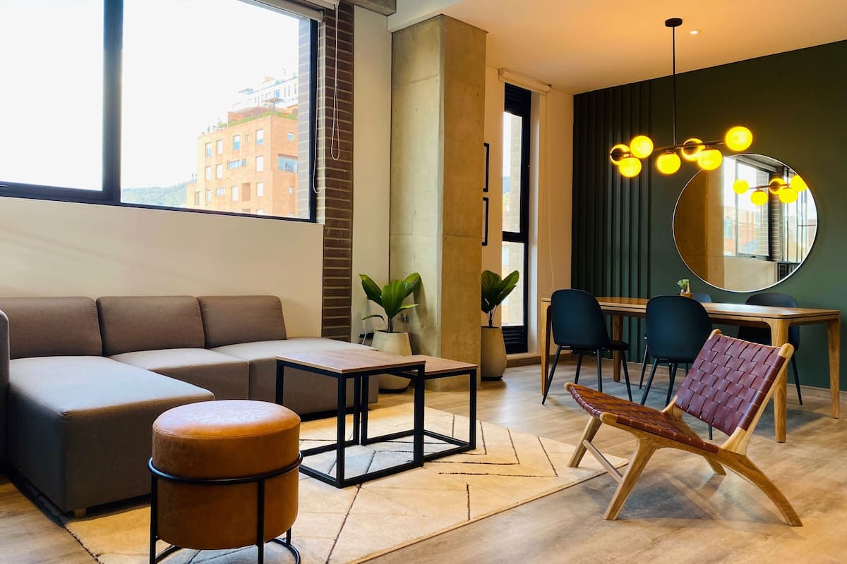 A modern living room with a sofa, ottoman, dining table, chairs, and a mirror.