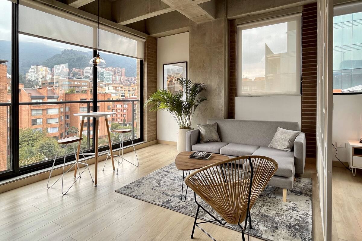 A modern living room with a large window, a sofa, a coffee table, and a wicker chair.