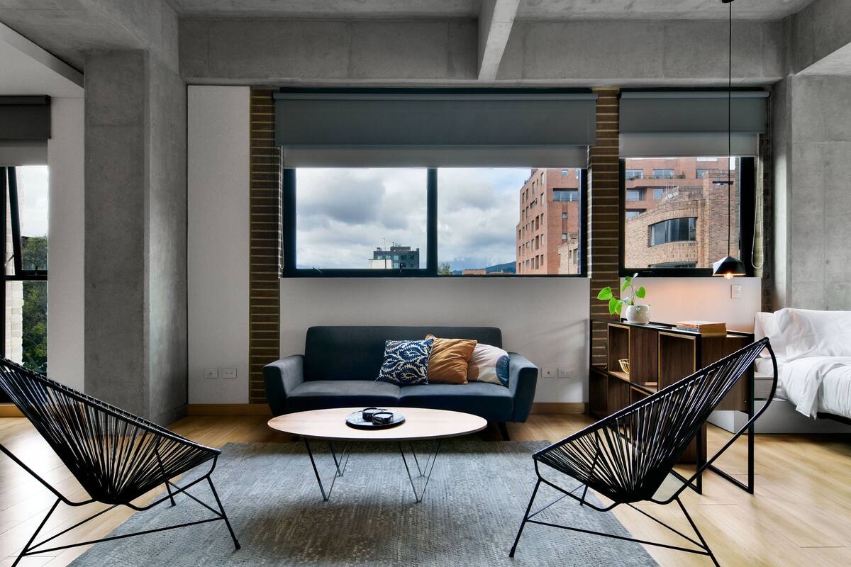 A modern living room with a sofa, two chairs, a coffee table, and a large window with a city view.