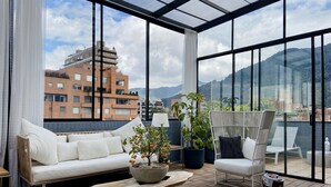 A modern balcony with a white sofa, a wooden coffee table, and potted plants. - Canvas by Wynwood House (Bogotá)