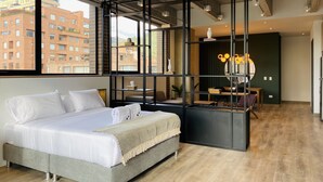 A modern bedroom with a large bed, a desk, and a view of the city. - Canvas by Wynwood House (Bogotá)
