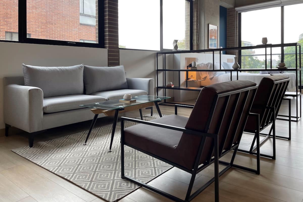 A modern living room with a grey sofa, a glass coffee table, and a patterned rug.