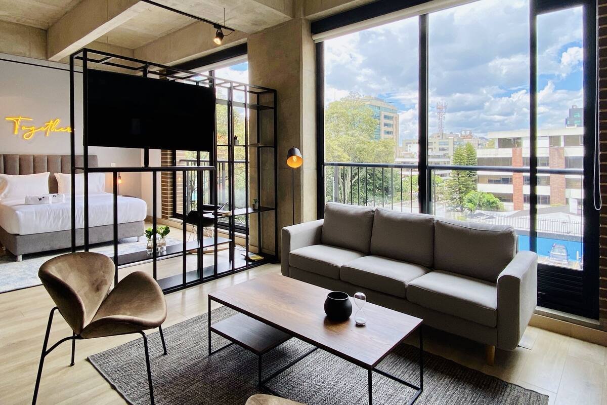 A modern hotel room with a large bed, a sofa, a coffee table, and a TV.