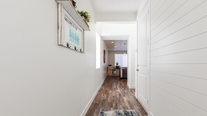 A hallway with wooden flooring, a rug, and a wall-mounted sign. - 3 bedrooms, no bunks! 2 Kings, 2 Queens | Lvl 2 EV Charger (Garden City)
