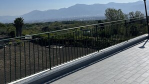 Un camí pavimentat amb barana metàl·lica que condueix a una vista de muntanyes llunyanes i un cel serè.