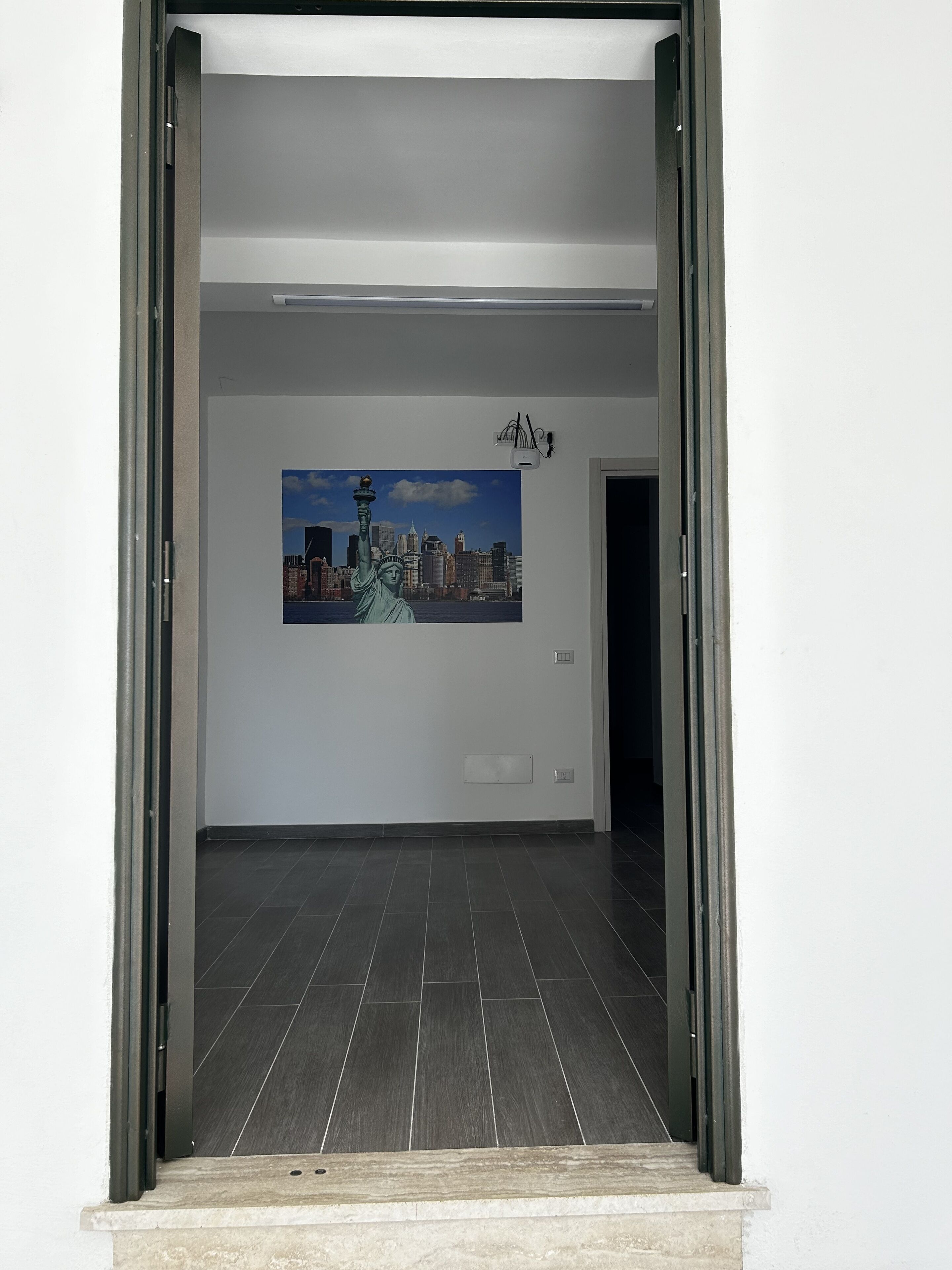 Een gang met een stadsgezichtschilderij aan de muur, een betegelde vloer en een deur naar een andere kamer.
