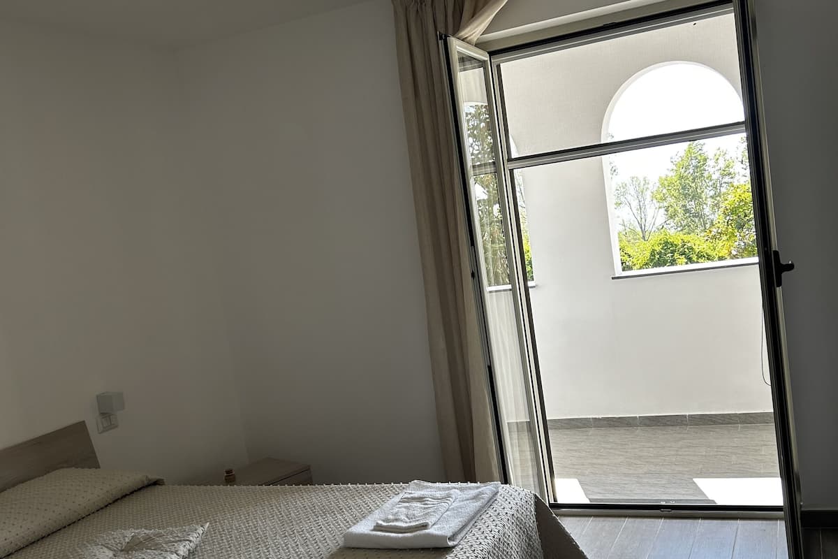 Un dormitorio con cama, mesita de noche y ventana con cortinas.