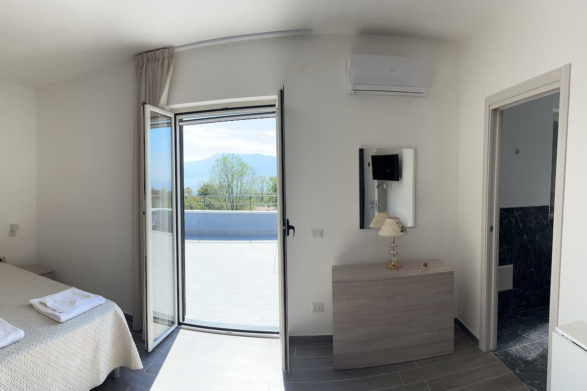 Una habitación de hotel con una cama, una mesita de noche con lámpara, un ventanal con vistas a un cañón y un equipo de aire acondicionado.