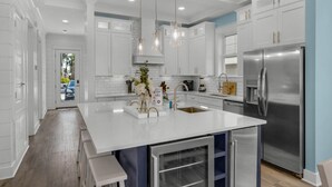 Une cuisine moderne avec des meubles blancs, un réfrigérateur en acier inoxydable et un îlot central doté d’un évier.