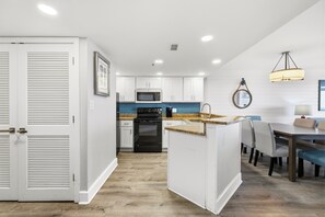 A modern kitchen with white cabinetry, a black oven, and a blue backsplash. - Family Oceanfront Condo Located in North end of Myrtle Beach! (Myrtle Beach)