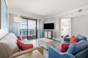 A hotel room with a balcony, a flat-screen TV, a sofa, a coffee table, and a bed.