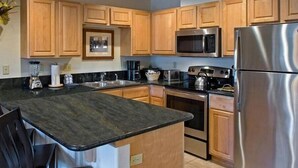 A modern kitchen with wooden cabinets, stainless steel appliances, and a granite countertop. - One-Bedroom Residence (Breckenridge)
