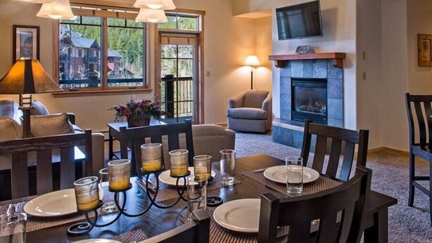 A dining area with a table set for four, a fireplace, and a television mounted on the wall. - One-Bedroom Residence (Breckenridge)