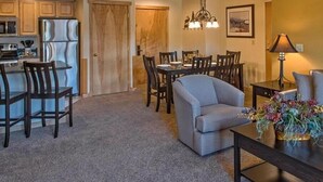 A modern kitchen with stainless steel appliances, a dining area with a gray sofa and wooden chairs, and a chandelier. - One-Bedroom Residence (Breckenridge)
