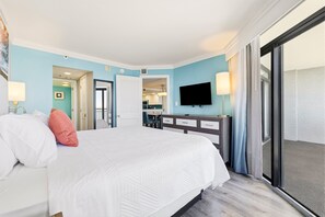 A hotel room with a bed, a desk, a television, and a view through a large window.