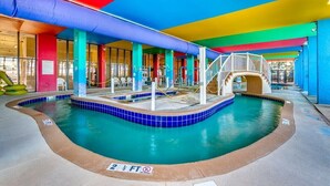 An indoor swimming pool with a 2 1/2 ft depth marker, surrounded by colorful pillars and a covered area with a staircase.