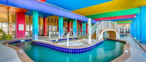 An indoor swimming pool with a 2 1/2 ft depth marker, surrounded by colorful pillars and a covered area with a staircase.