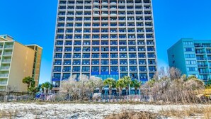 A multi-story hotel with a central atrium, balconies, and a beach view.