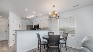 A modern kitchen with white cabinets, a central island, and a dining area with four chairs.
