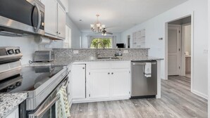 A modern kitchen with white cabinetry, granite countertops, stainless steel appliances, and a central island.