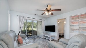A living room with a ceiling fan, a flat-screen TV, and a sliding glass door leading to a patio.