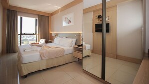Quarto de hotel com uma cama grande, mesa de cabeceira, espelho e janela com cortinas.