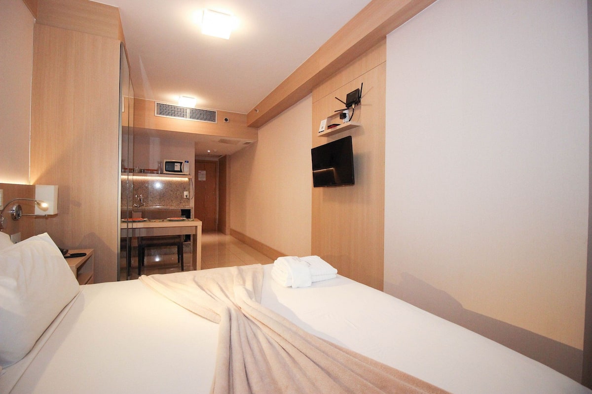 A hotel room with a bed, a desk, a microwave, and a TV.