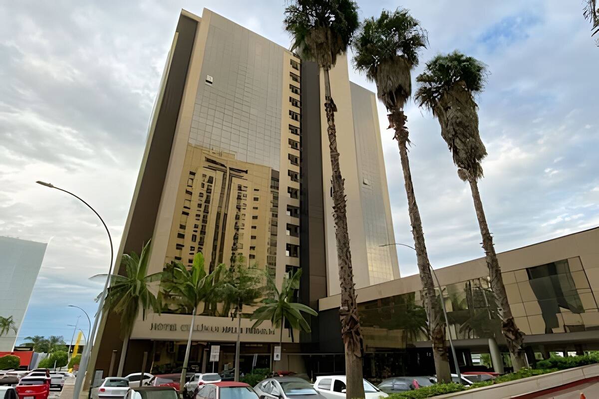 A tall hotel building with multiple floors, palm trees in front, and a clear sky.