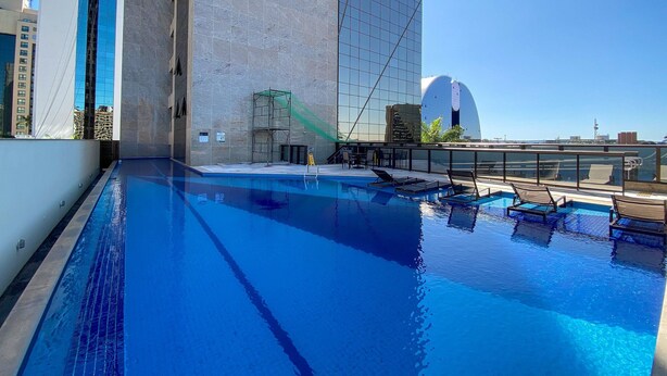Uma piscina no terraço com água azul cristalina, rodeada por edifícios modernos e um céu limpo.