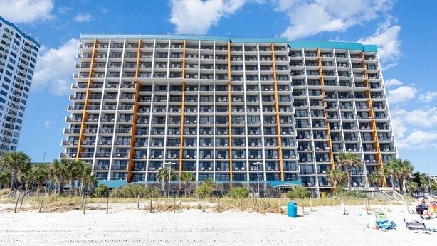 Un hotel de varios pisos con diseño moderno, con balcones y vistas a la playa.