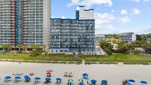 Ein Strandhotel mit mehreren Balkonen, einem Poolbereich und Strandsonnenschirmen.