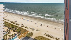 Blick auf den Strand vom Hotelbalkon, mit Pool und Sandstrand.