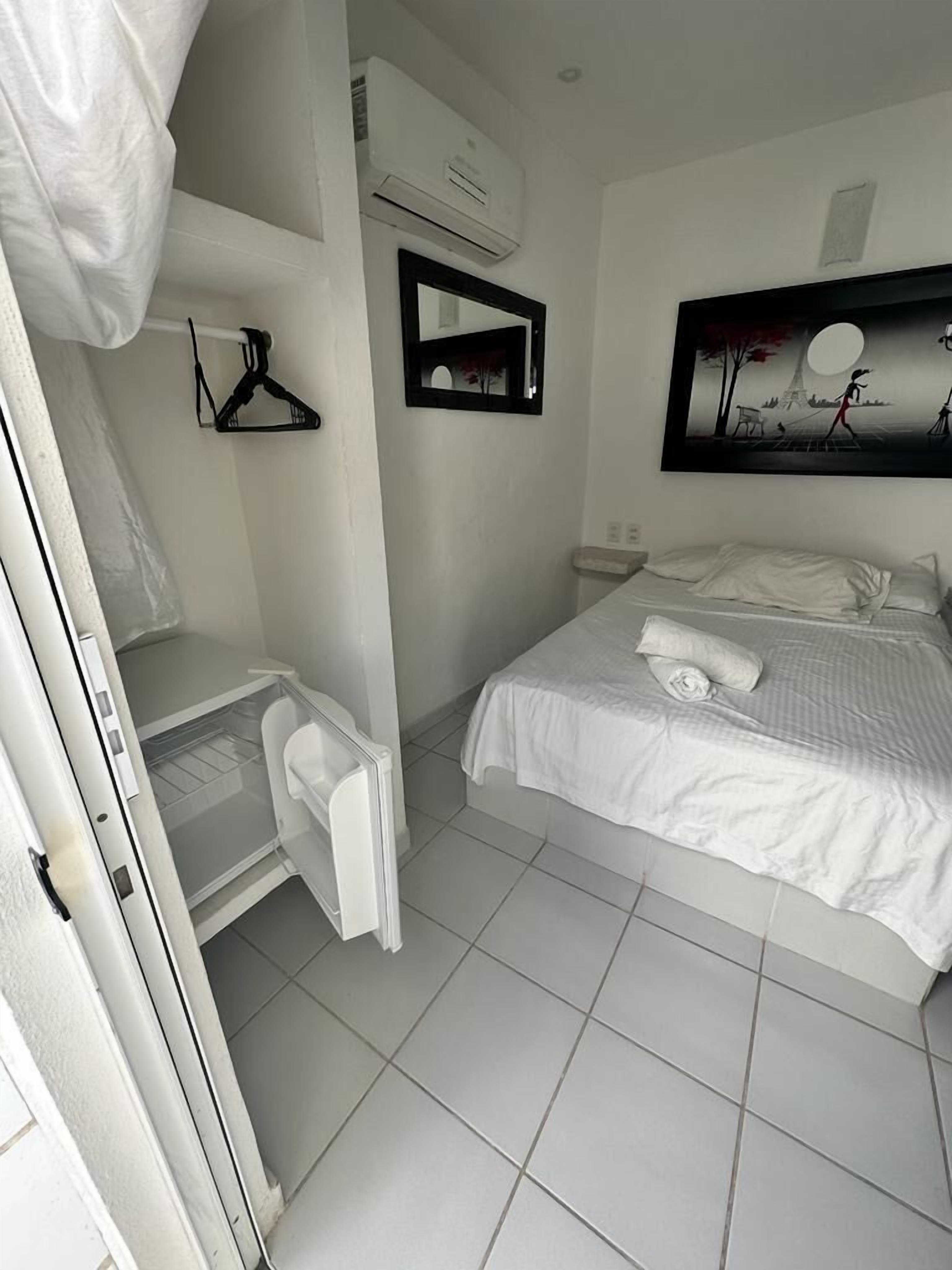 A bedroom with a bed, a hanging clothes rack, a mirror, and an air conditioning unit.