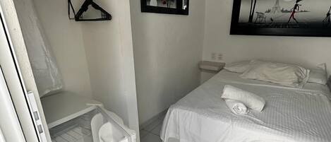A bedroom with a bed, a hanging clothes rack, a mirror, and an air conditioning unit.