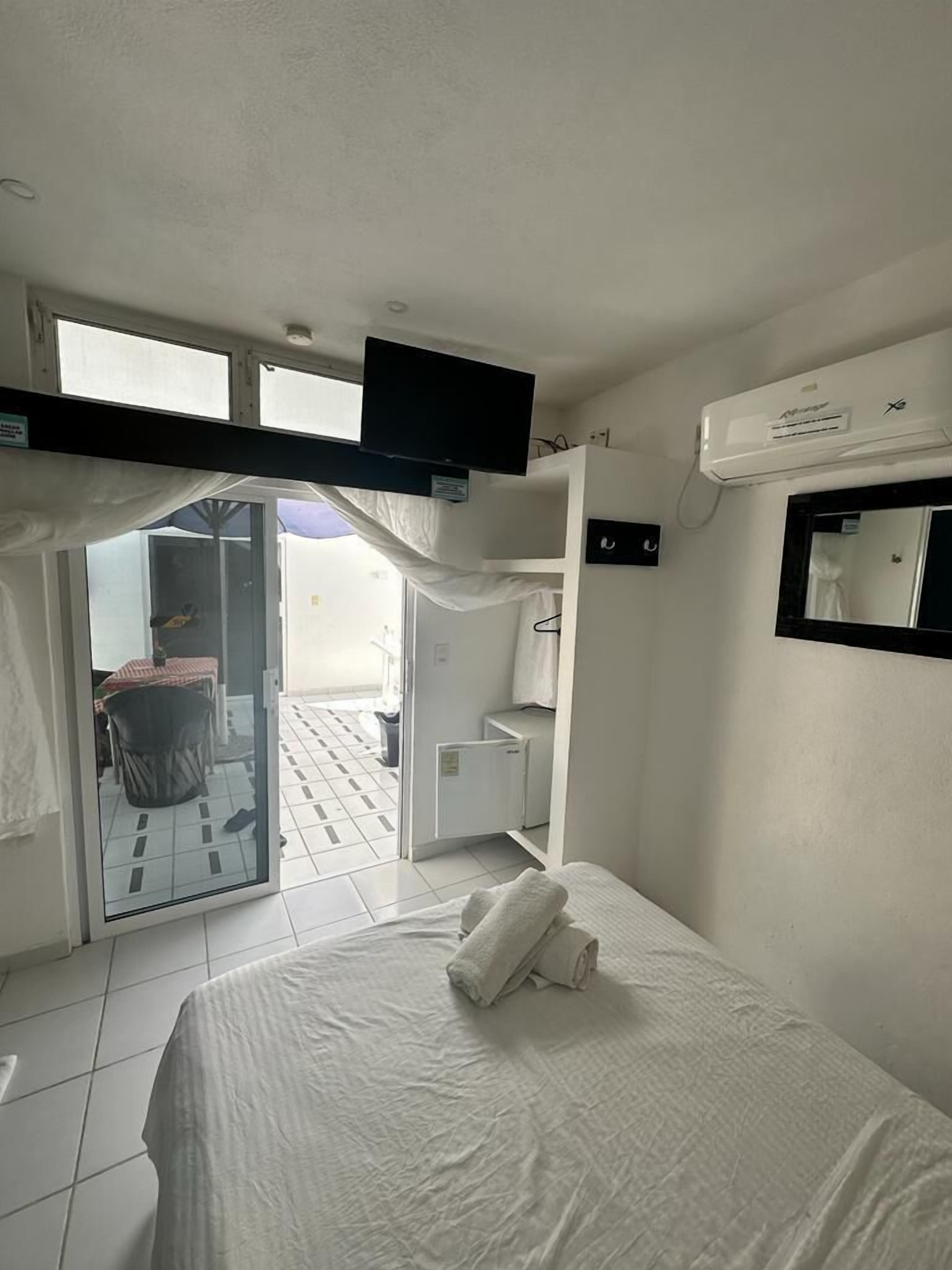 A hotel room with a bed, a TV, an air conditioner, and a sliding door leading to a balcony.