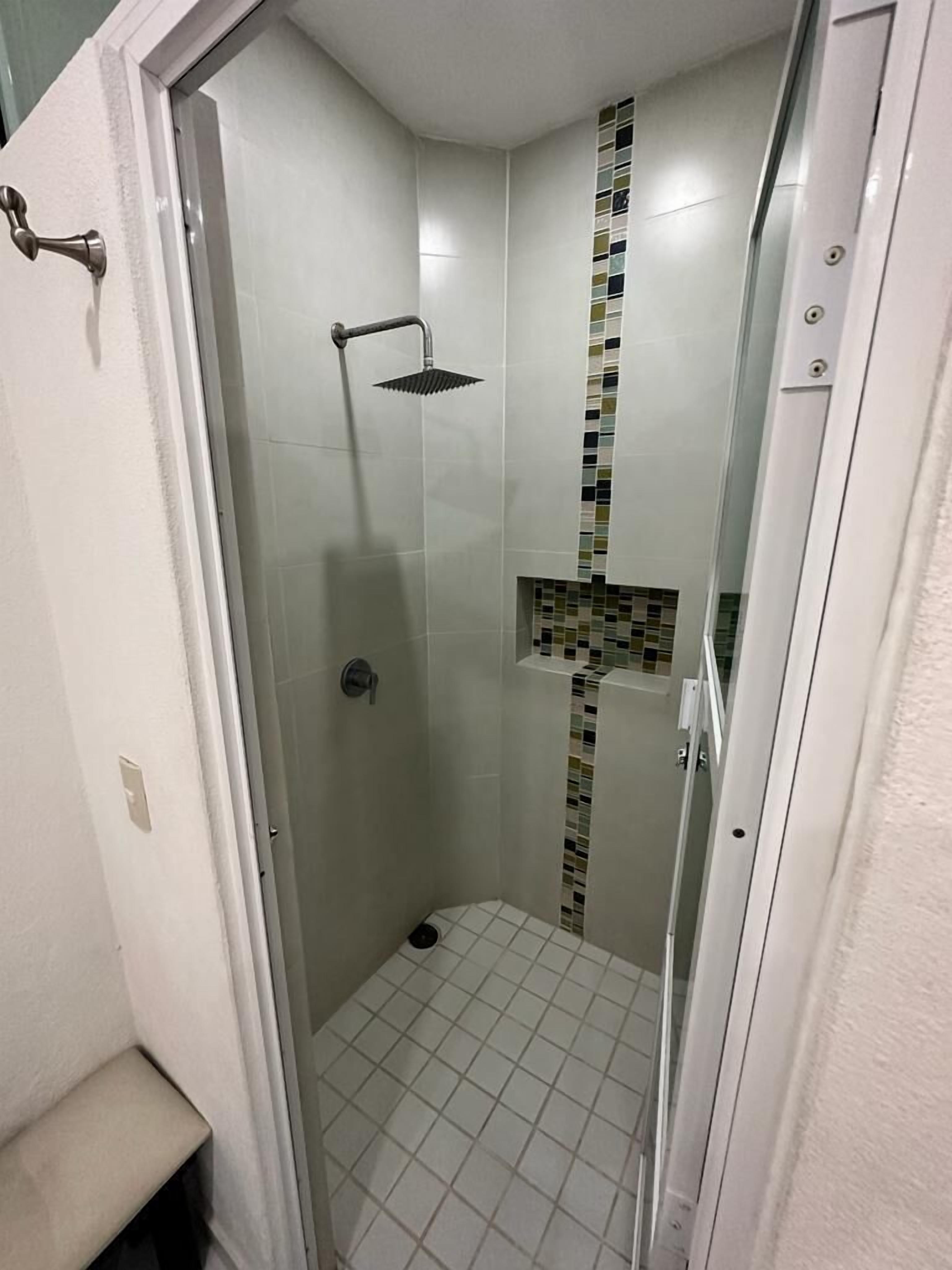 Un piccolo bagno doccia chiuso, con pavimento piastrellato e un motivo a mosaico sulla parete.