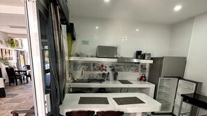 Una cocina moderna con encimeras blancas, una zona de comedor con dos sillas de madera y un refrigerador.