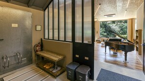 A modern interior with a private door, a bench with slippers, a piano, and a view of greenery outside.