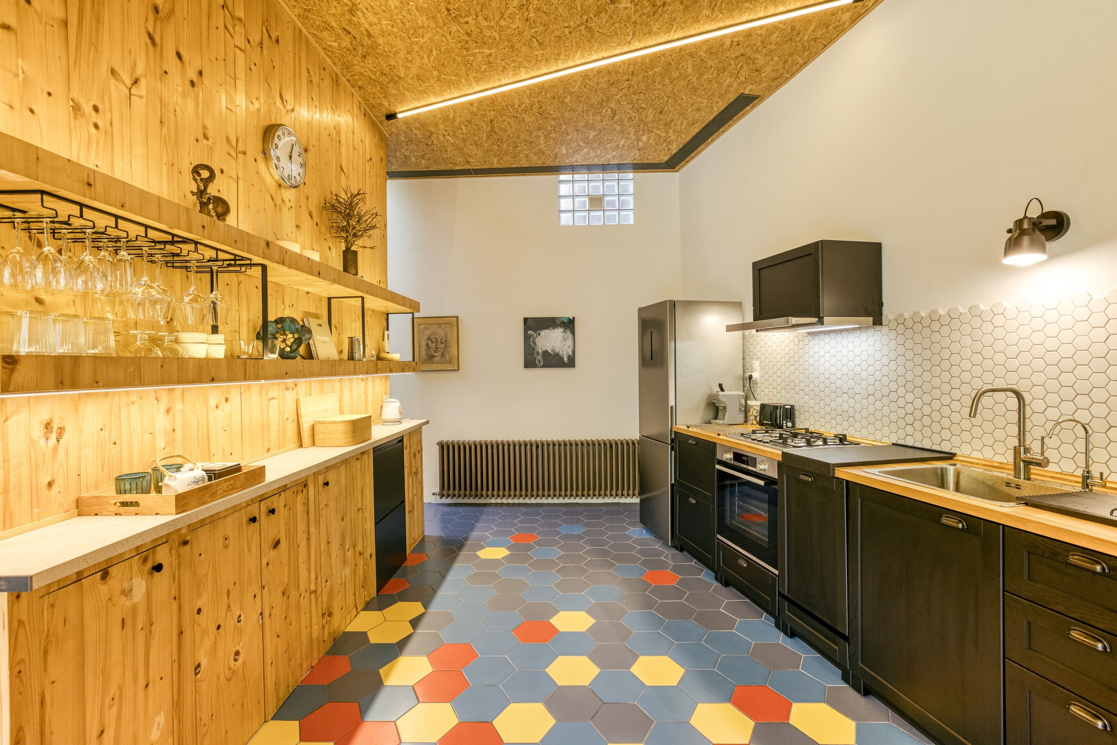 Una cocina con armarios de madera, un refrigerador de acero inoxidable, un lavamanos y un llamativo patrón de suelo hexagonal.