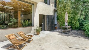 A modern outdoor patio with lounge chairs, a table, and a potted plant.