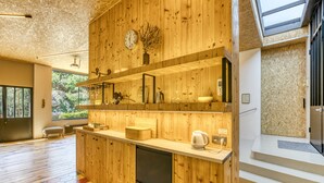 A modern kitchen with wooden cabinetry, a built-in coffee maker, and a large window overlooking greenery.