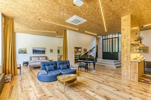 Un vaste espace de vie comprenant un canapé bleu, une table basse, un piano et une bibliothèque.