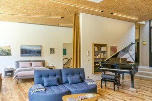 Un salon moderne comprenant un grand piano, un canapé, un lit et une bibliothèque.