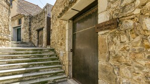 A stone building with a metal door, a sign reading 'eSpaL'temps,' and a staircase leading to an entrance.