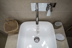 A sleek bathroom sink with a chrome faucet and mirror, accompanied by a woven basket and a ceramic mug.