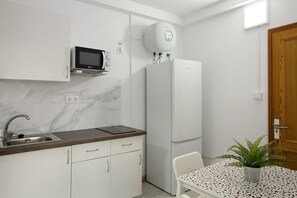 A compact kitchen with a sink, microwave, refrigerator, and a small dining table with a plant.