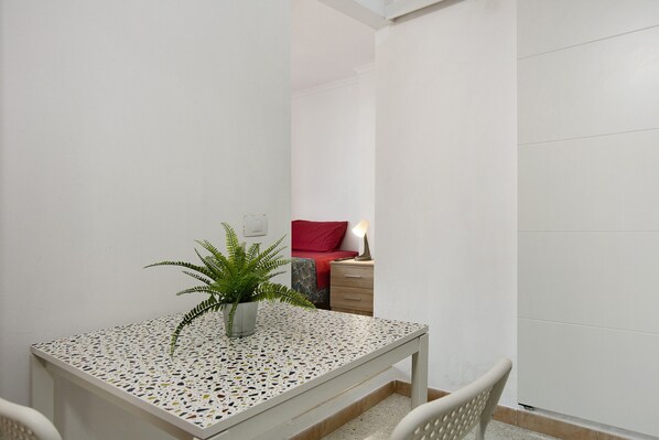 Une petite pièce avec une table blanche, une plante en pot, un coussin rouge et une lampe de chevet.