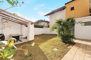 A backyard with a patio, a small table, a palm tree, and a white building.